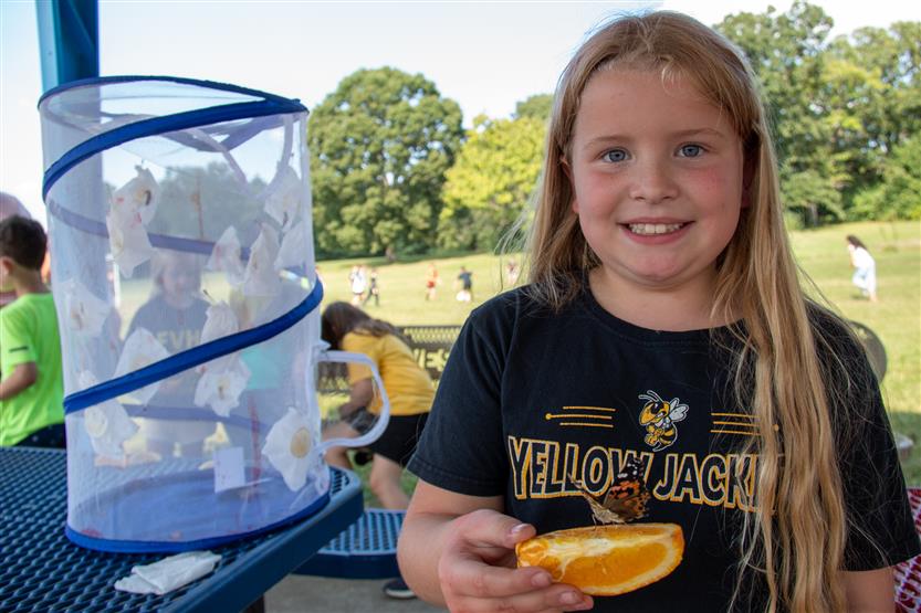 A girl with long blonde hair holds an orange slice with a butterfly